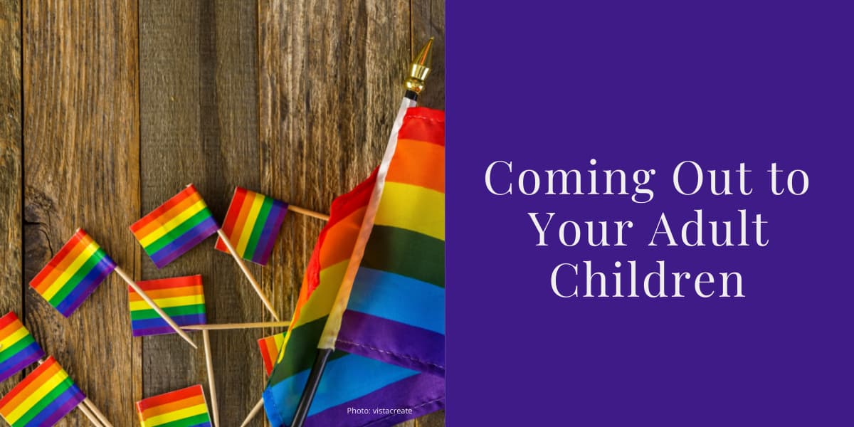 An assortment of small pride rainbow flags lie scattered on a wooden table. Tho the right of this photo, text on a purple background reads: Coming Out to Your Adult Children
