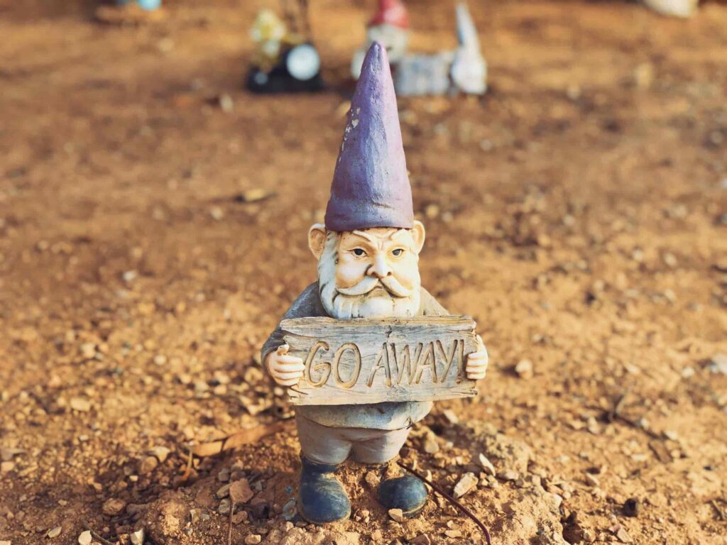A garden gnome wearing a purple pointy hat holding a sign that reads "GO AWAY". Discrimination and prejudice can be a part of culture shock.