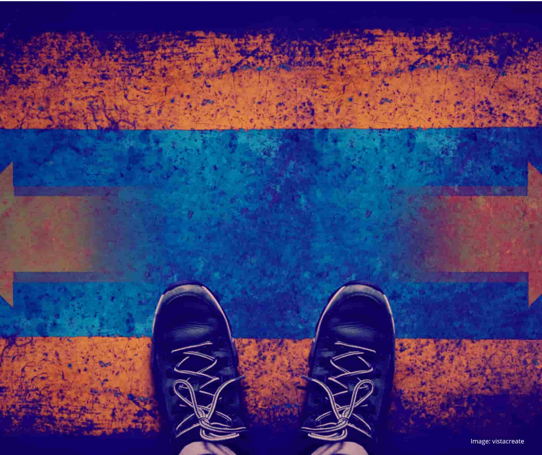 A pair of lace up trainers on a painted floor. Two arrow are painted on the floor, one points to the left of the image, the other pointing to the right.