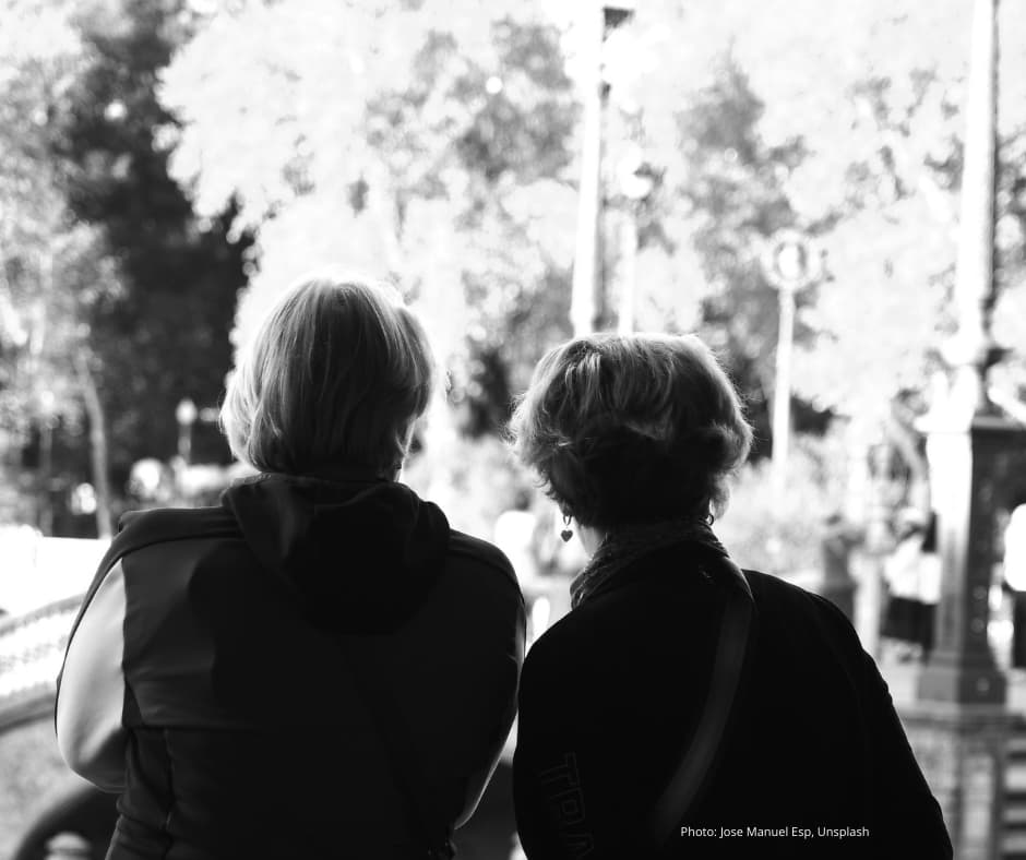 A black and white photo of what we might assume to be the backs of two middle aged women looking out into a park or garden.