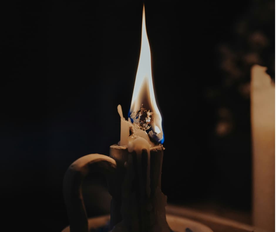 Lit candle burning brightly in dark room but almost burnt out