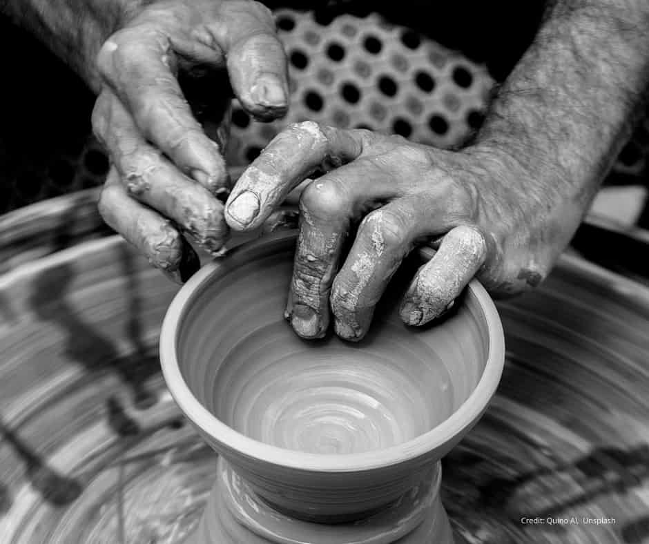 Potters hands shaping clay Close-up black and white photo of a potter’s hands shaping a clay pot on a spinning pottery wheel. The hands are coated in wet clay as they carefully form the rim of the vessel.