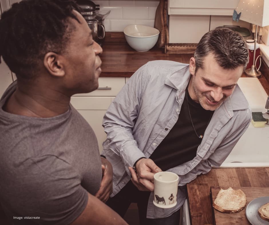 Two men, probably in their 40s, seem to be enjoying one another's company in a kitchen, perhaps chatting over a coffee.